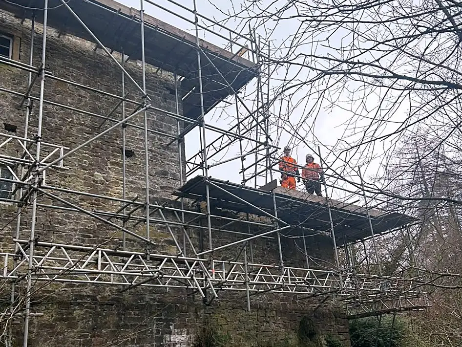 TNT scaffolders on a boarded platform around a stone structure
